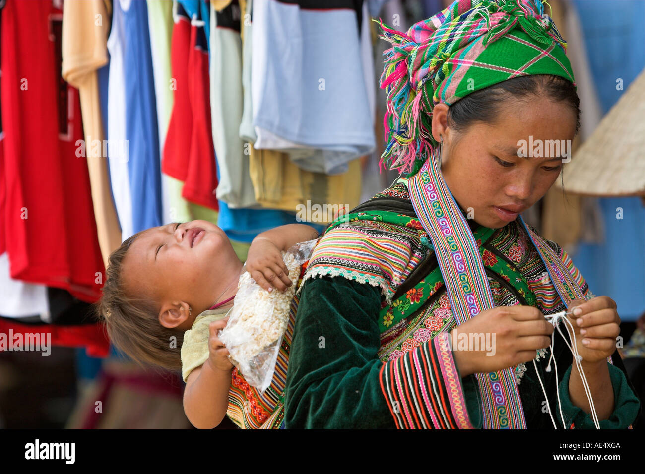 Jeune femme avec bébé en sling Bac Ha marché hilltribe Hmong fleurs colorées de traders nord Vietnam Banque D'Images