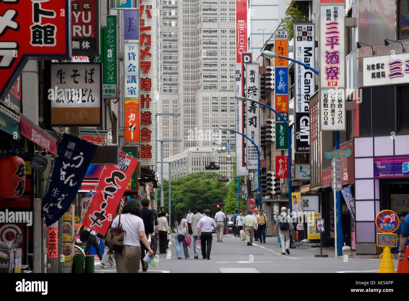 Les gens marcher dans une rue avec de nombreux signes japonais de l'électronique de vente et d'autres éléments dans le quartier de Shinjuku de Tokyo Japon Banque D'Images