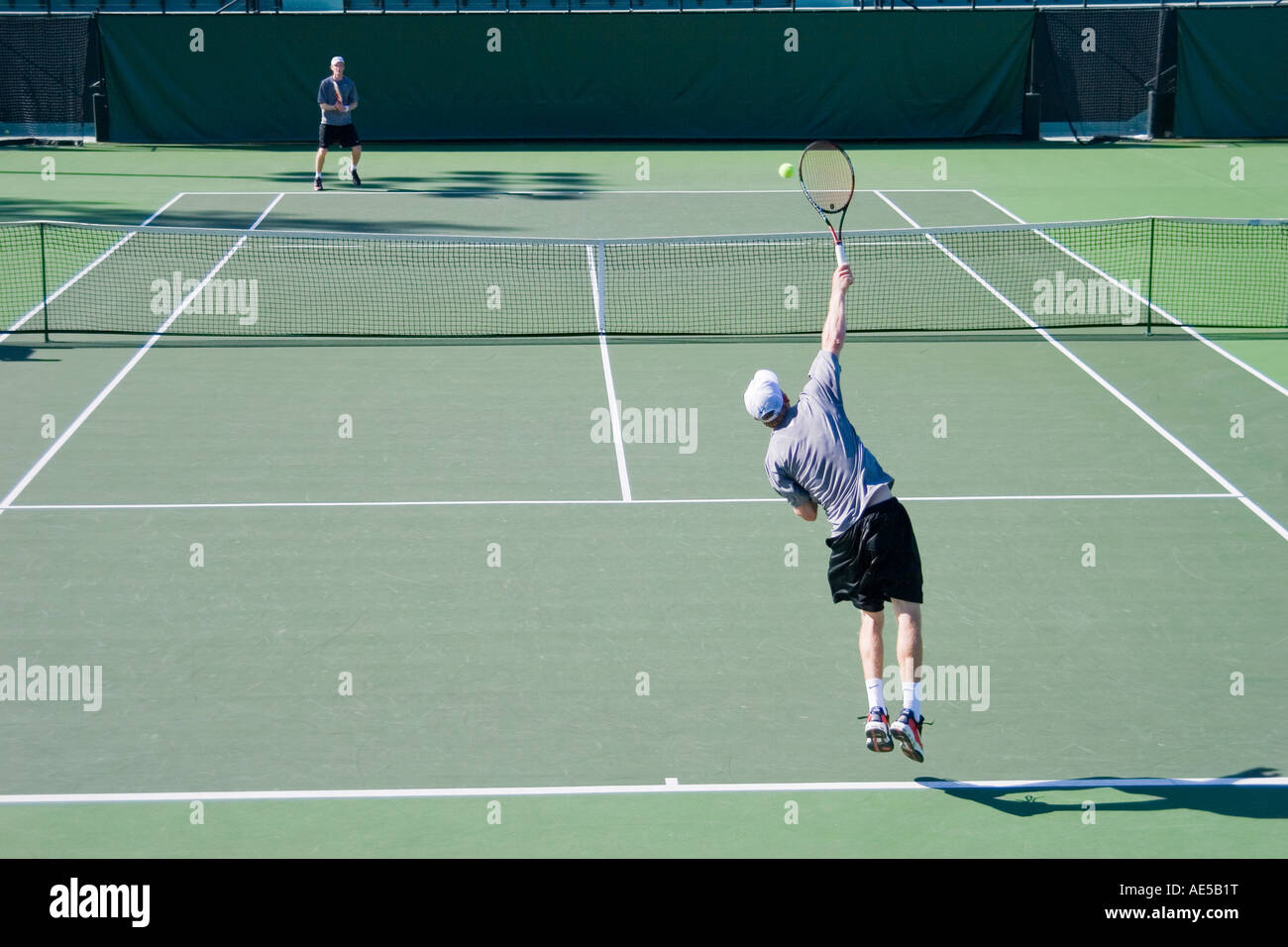 Deux hommes dans leur 20s à jouer au tennis sur un stade de tennis avec un homme d'atteindre et de servir la balle saut Banque D'Images