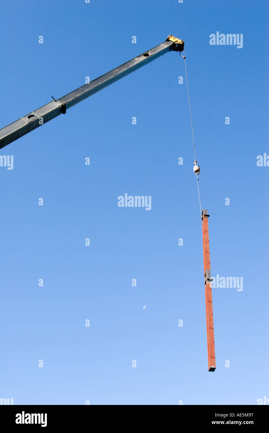 D'une grue bras étendu et l'abaissement du crochet de poutres en acier, avec la lune dans le ciel sur un site de construction Banque D'Images