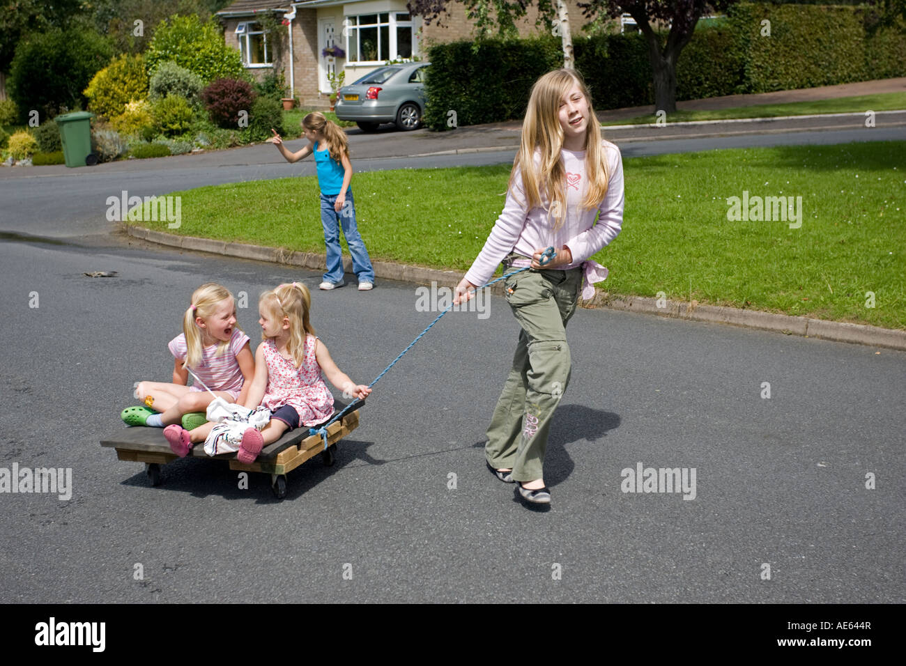 Les filles s'amusant tirant plus jeunes sœurs le long de la route sur chariot maison UK Banque D'Images