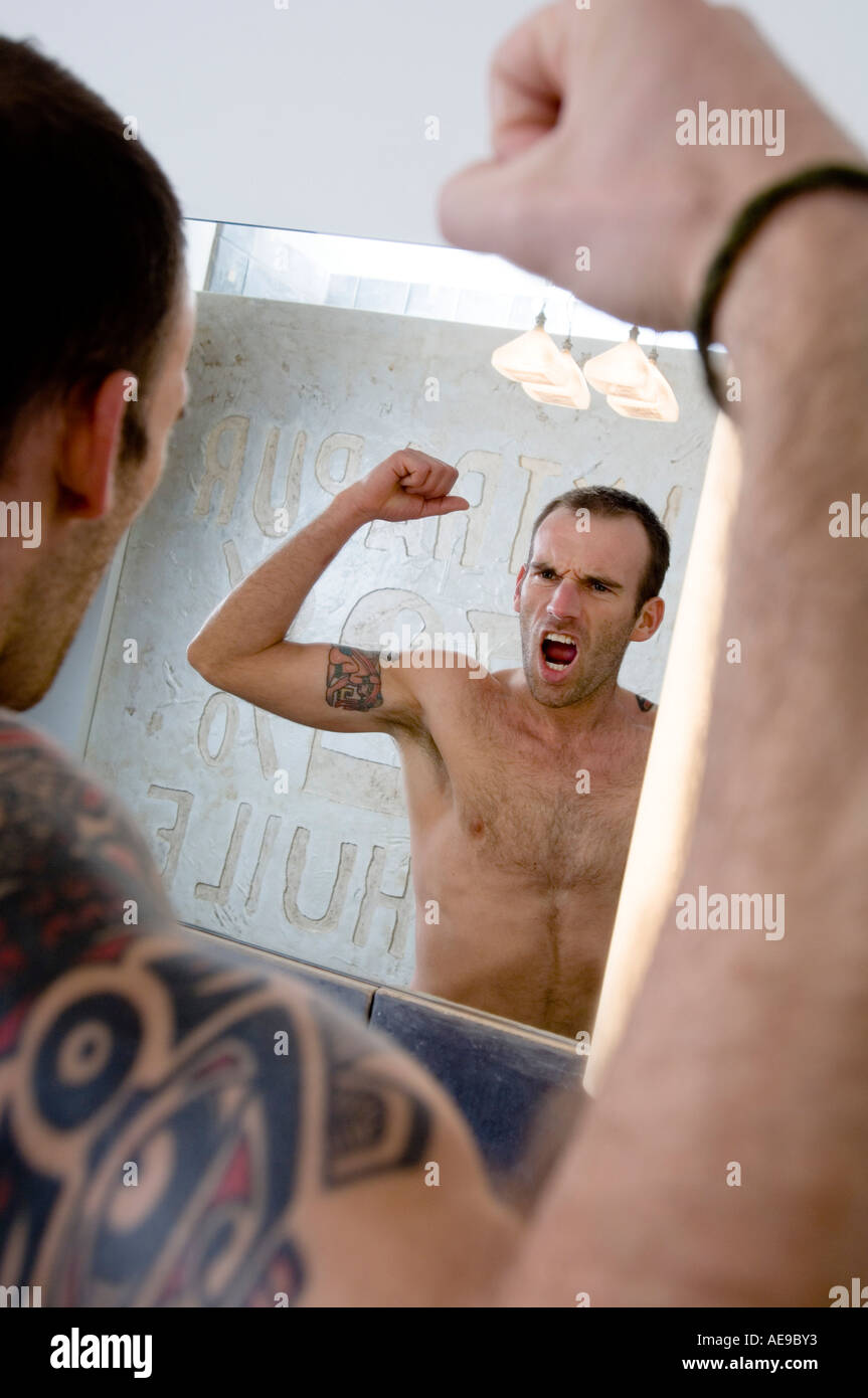 Tattooed man flexing muscles en face de miroir de salle de bains Banque D'Images