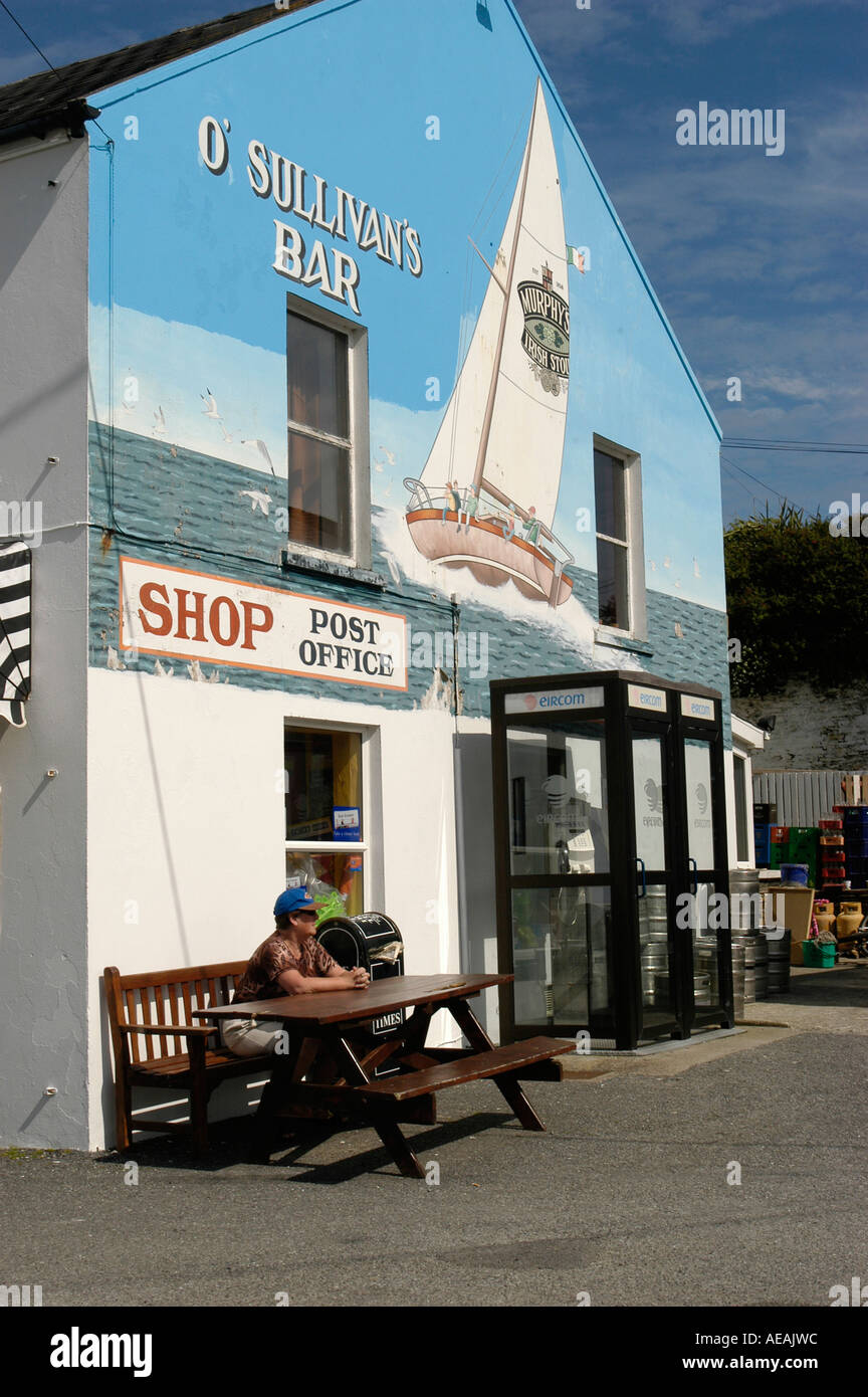 Un homme assis à table à l'extérieur O'Sullivan's Bar shop et bureau de poste Crookhaven , Comté de Cork au sud ouest de l'Irlande Banque D'Images
