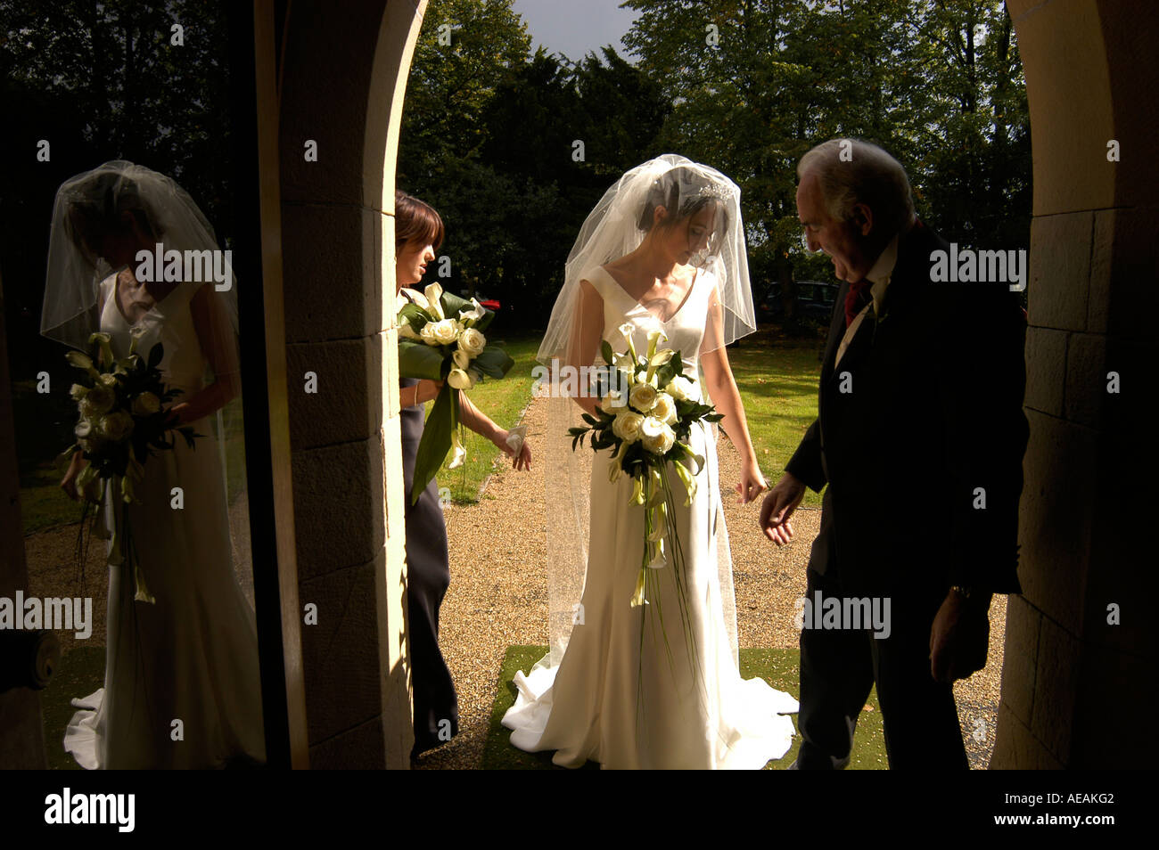 Jeune mariée avec son père juste avant qu'elle entre dans l'église pour rencontrer le marié avec son reflet dans la porte en verre Banque D'Images