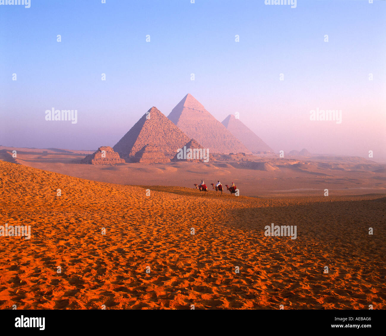 Pyramides et trois membres d'une tribu bédouine sur les chameaux au lever du soleil, Giza, Le Caire, Egypte Banque D'Images