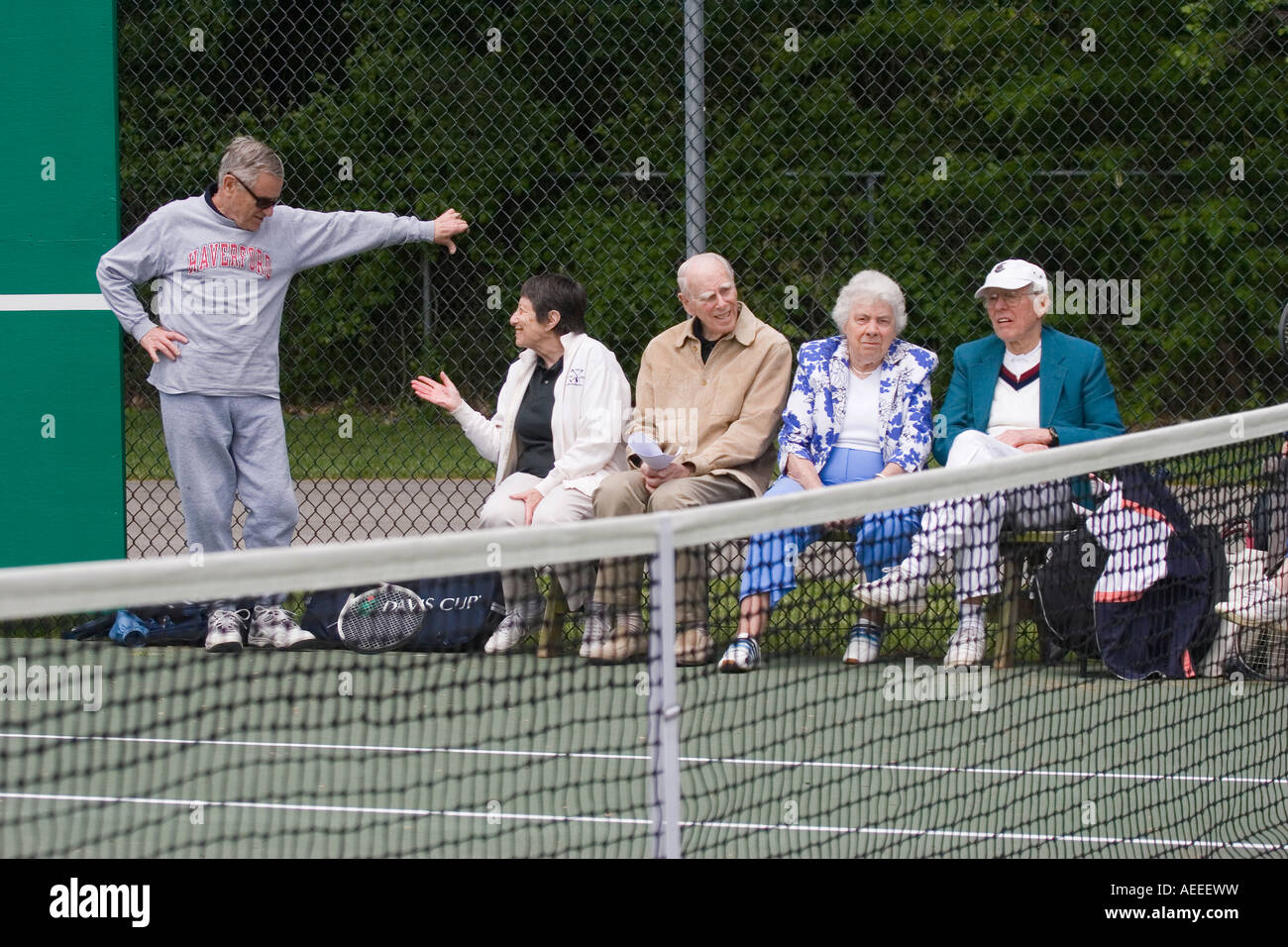 Les hommes âgés et les femmes assises sur les bancs à côté d'un court de tennis à regarder un match en cours et le chat Banque D'Images