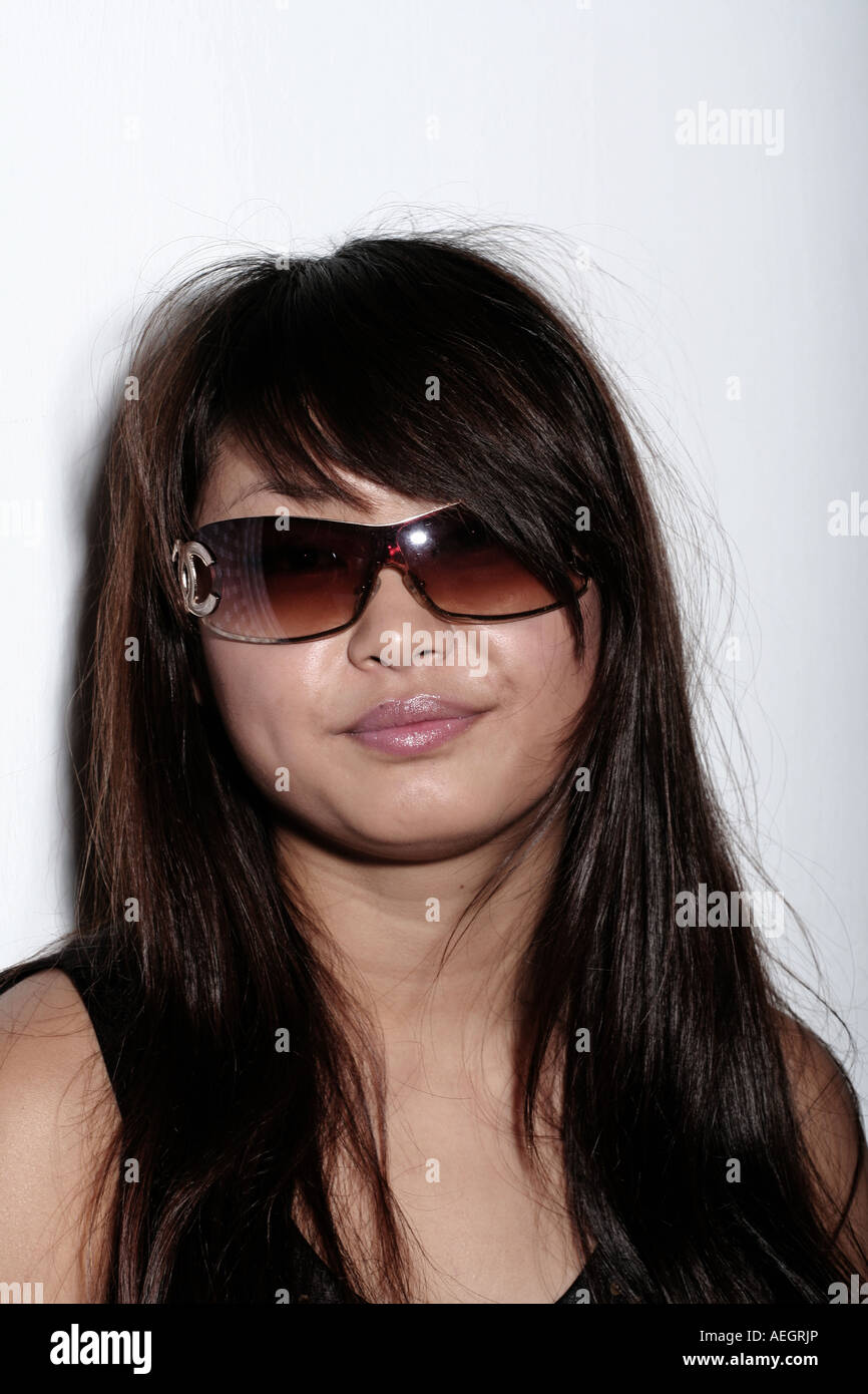 Portrait en gros plan d'une femme portant des lunettes de soleil foncées élégantes avec de longs cheveux foncés sur un fond blanc Uni. Banque D'Images
