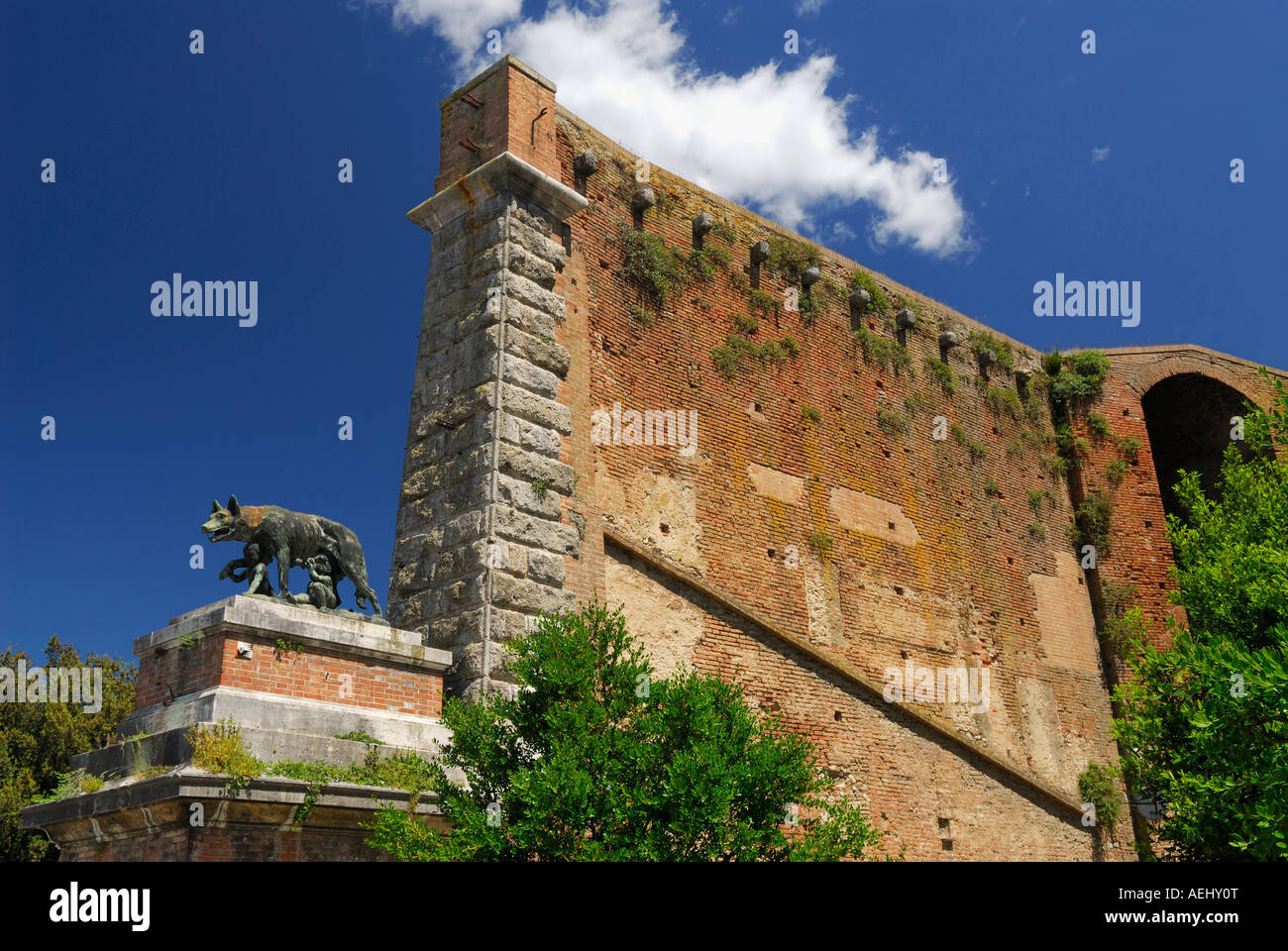 Ancien mur et la porte dans la vieille ville de Sienne Toscane Italie avec statue romaine de Romulus et Remus suckling elle wolf avec ciel bleu Banque D'Images