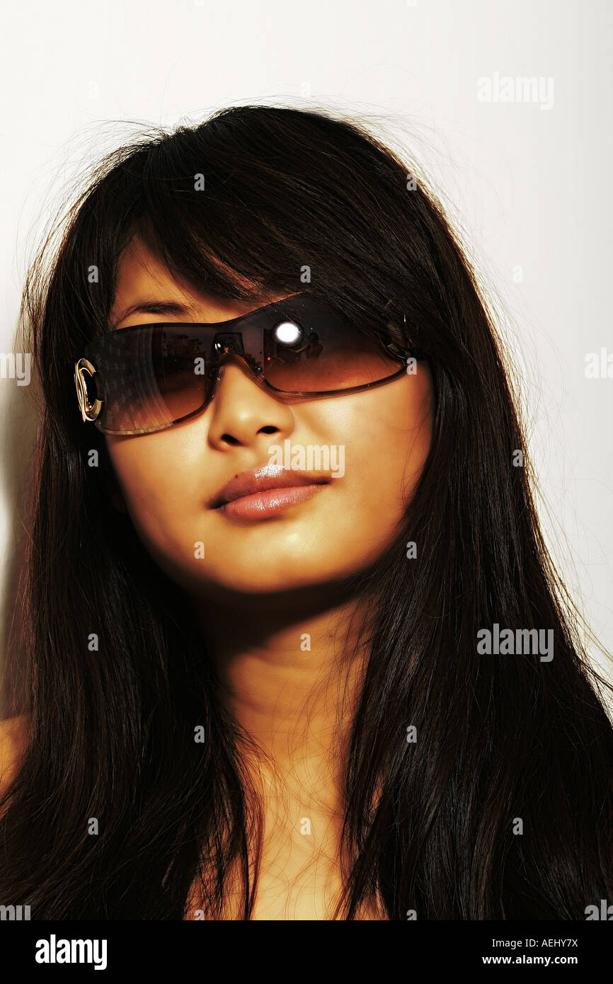 Portrait en gros plan d'une femme portant des lunettes de soleil foncées élégantes avec de longs cheveux foncés sur un fond blanc Uni. Banque D'Images