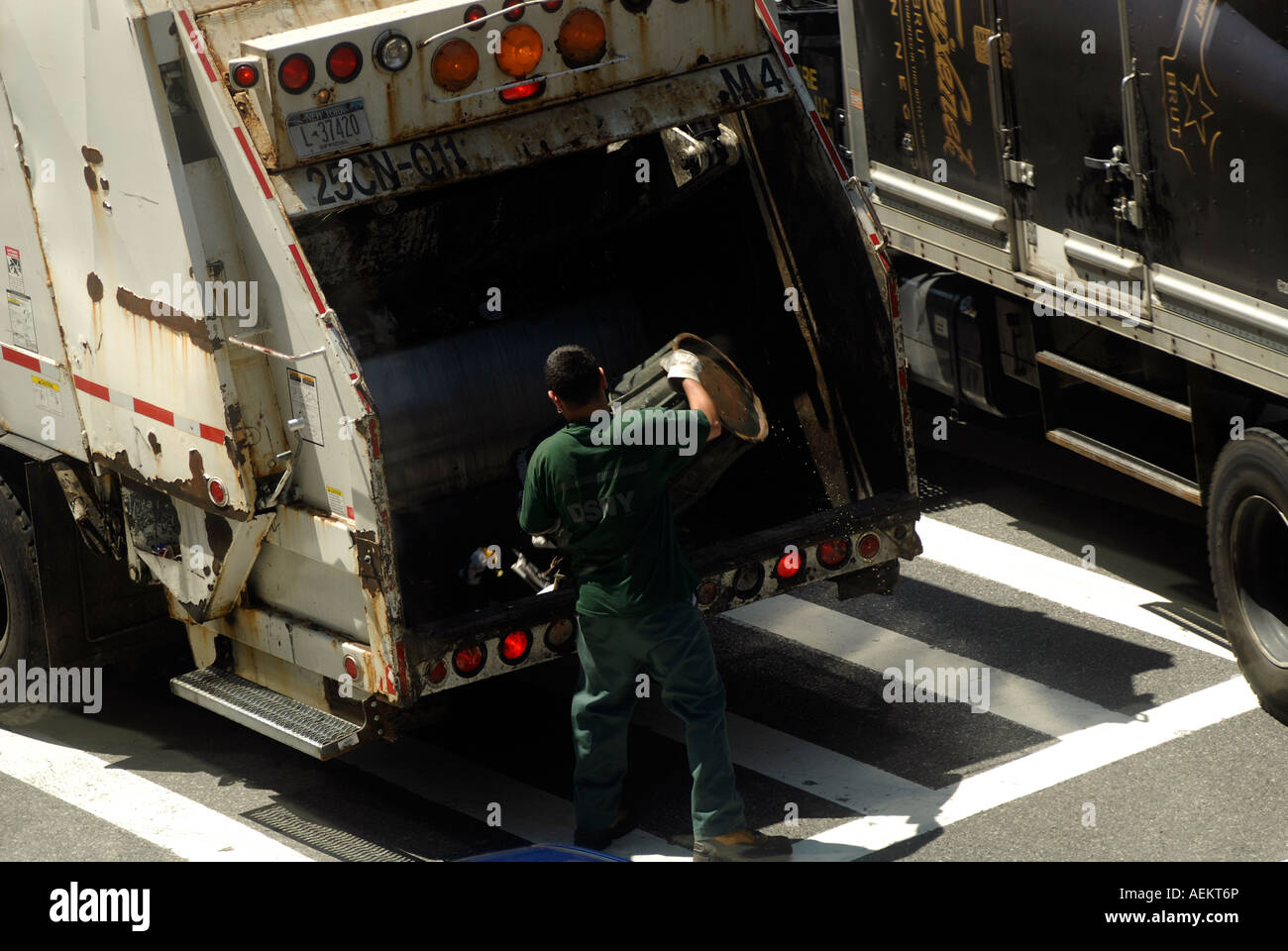 Un NYC Department of Sanitation worker se vide une corbeille à l'arrière d'un camion à ordures Banque D'Images