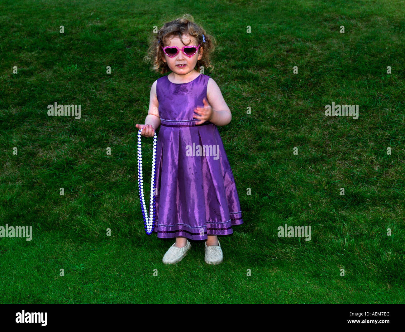 Trois ans, fille d'une robe de taffetas de soie pourpre à une réception de mariage dans un jardin avec des colliers de perles Banque D'Images