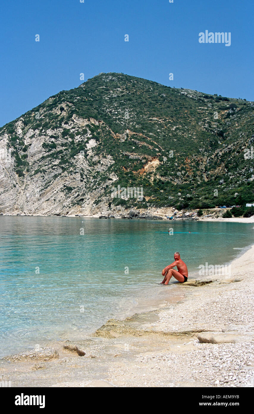 Homme assis au bord de l'eau, la baie de Petani, Kefalonia, Grèce, Petani Banque D'Images