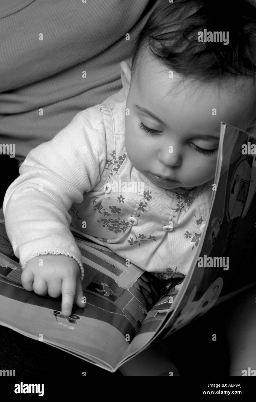 Tourné en noir et blanc d'un bébé en montrant une photo dans un livre, et assis sur son genou Banque D'Images