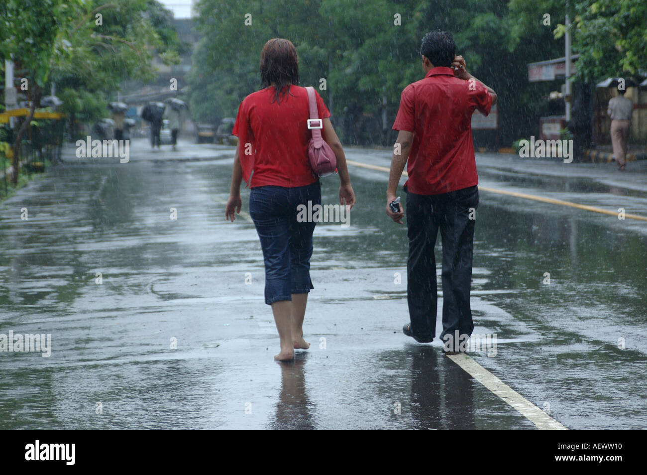 Couple, homme et femme portant tous deux un t-shirt rouge, marchant sous la pluie de mousson, Bombay, Mumbai, Maharashtra, Inde, Asie Banque D'Images