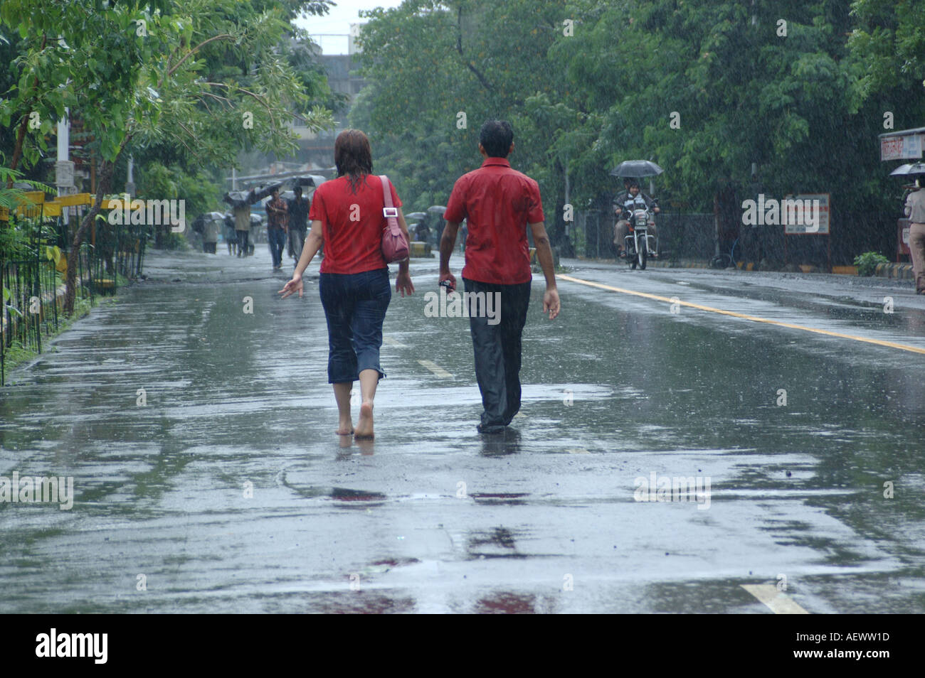 Couple, homme et femme portant tous deux un t-shirt rouge, marchant sous la pluie de mousson, Bombay, Mumbai, Maharashtra, Inde, Asie Banque D'Images