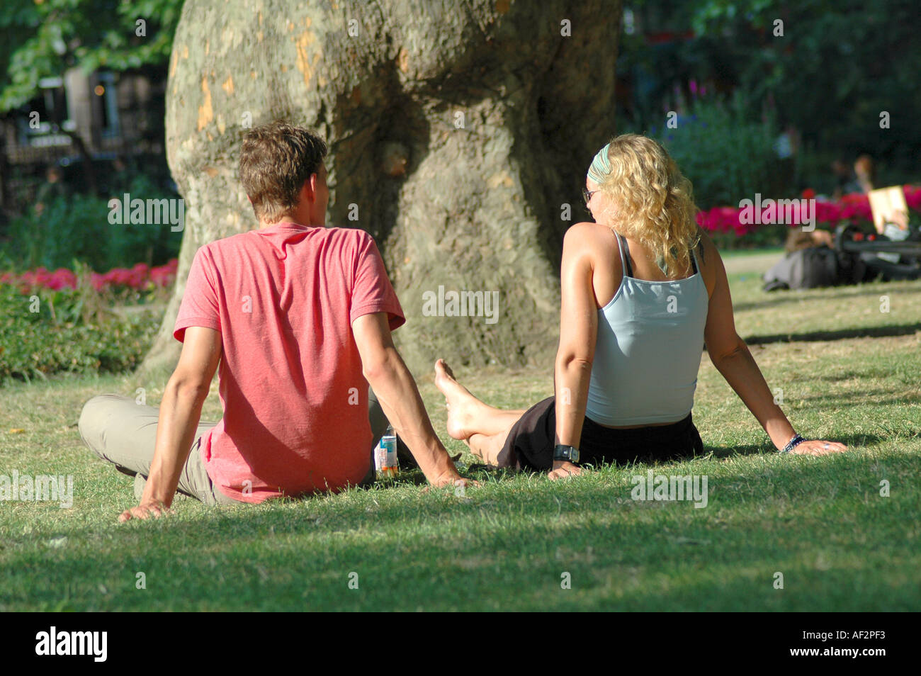 Tourist couple assis sur l'herbe dans un parc du centre de Londres en été Banque D'Images