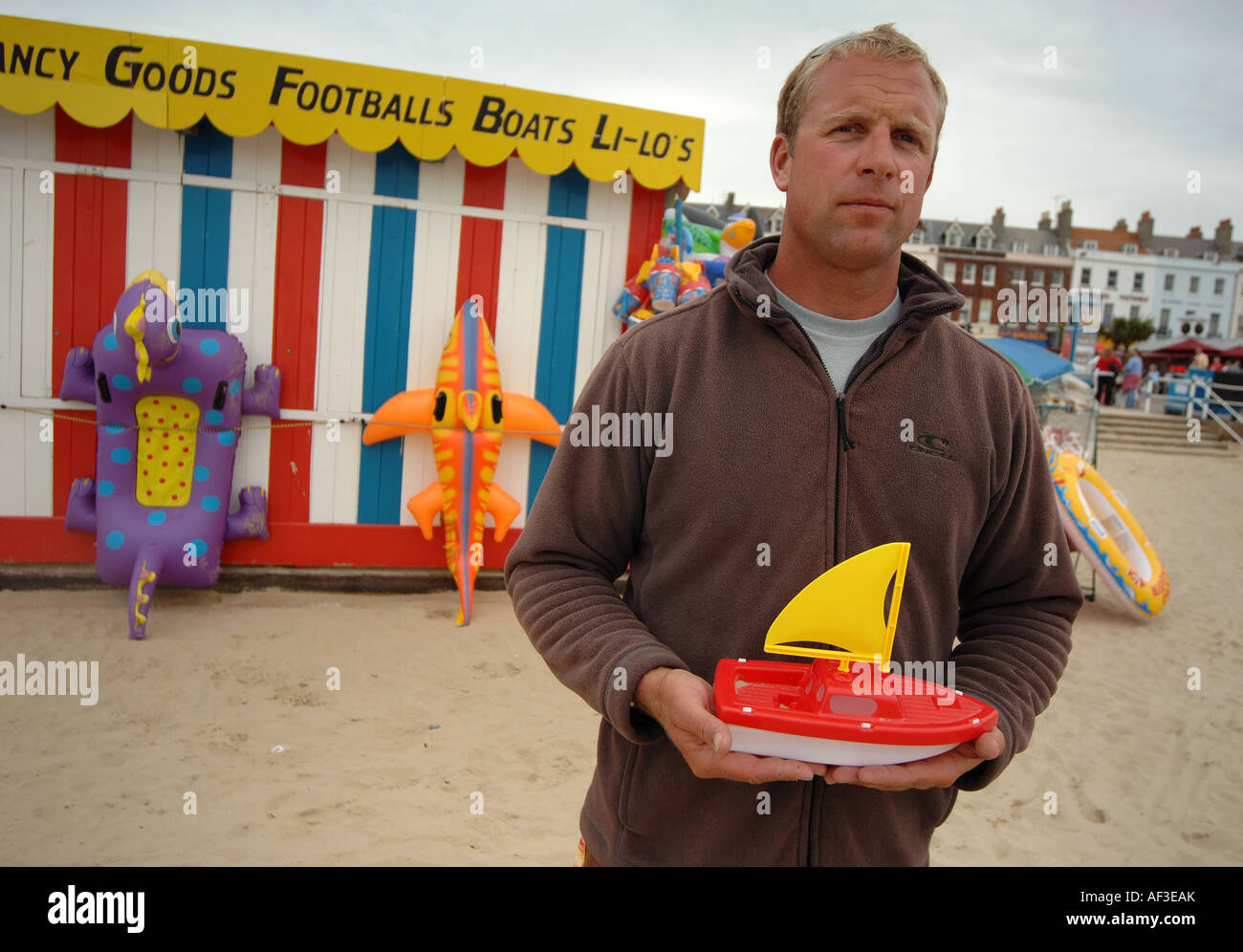 Un homme sur la plage de Weymouth, dans le Dorset, tenant un petit bateau à voile plastuc Banque D'Images