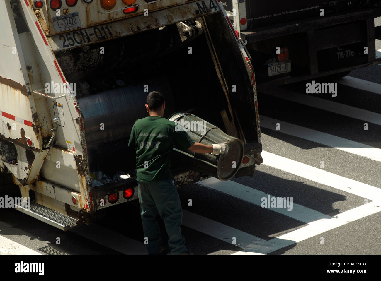 Un NYC Department of Sanitation worker se vide une corbeille à l'arrière d'un camion à ordures Banque D'Images