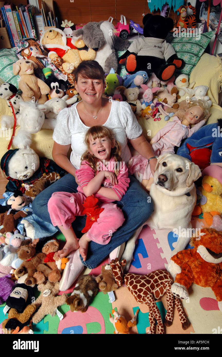 Smiling mother avec cinq ans fille blonde sur ses genoux entourés par des peluches et chien Banque D'Images