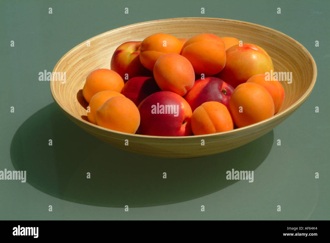 Bol en bambou rempli d'abricots et nectarines sur fond de verre vert Banque D'Images