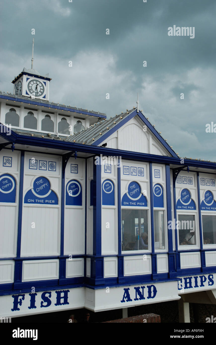 Poisson et chip shop signe sur la jetée d''Eastbourne avec un ciel menaçant au-dessus Banque D'Images