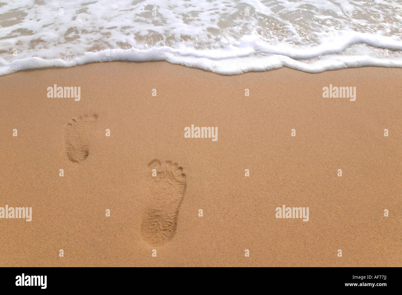 Empreintes de pas sur une plage de sable fin de disparaître dans la mer Banque D'Images