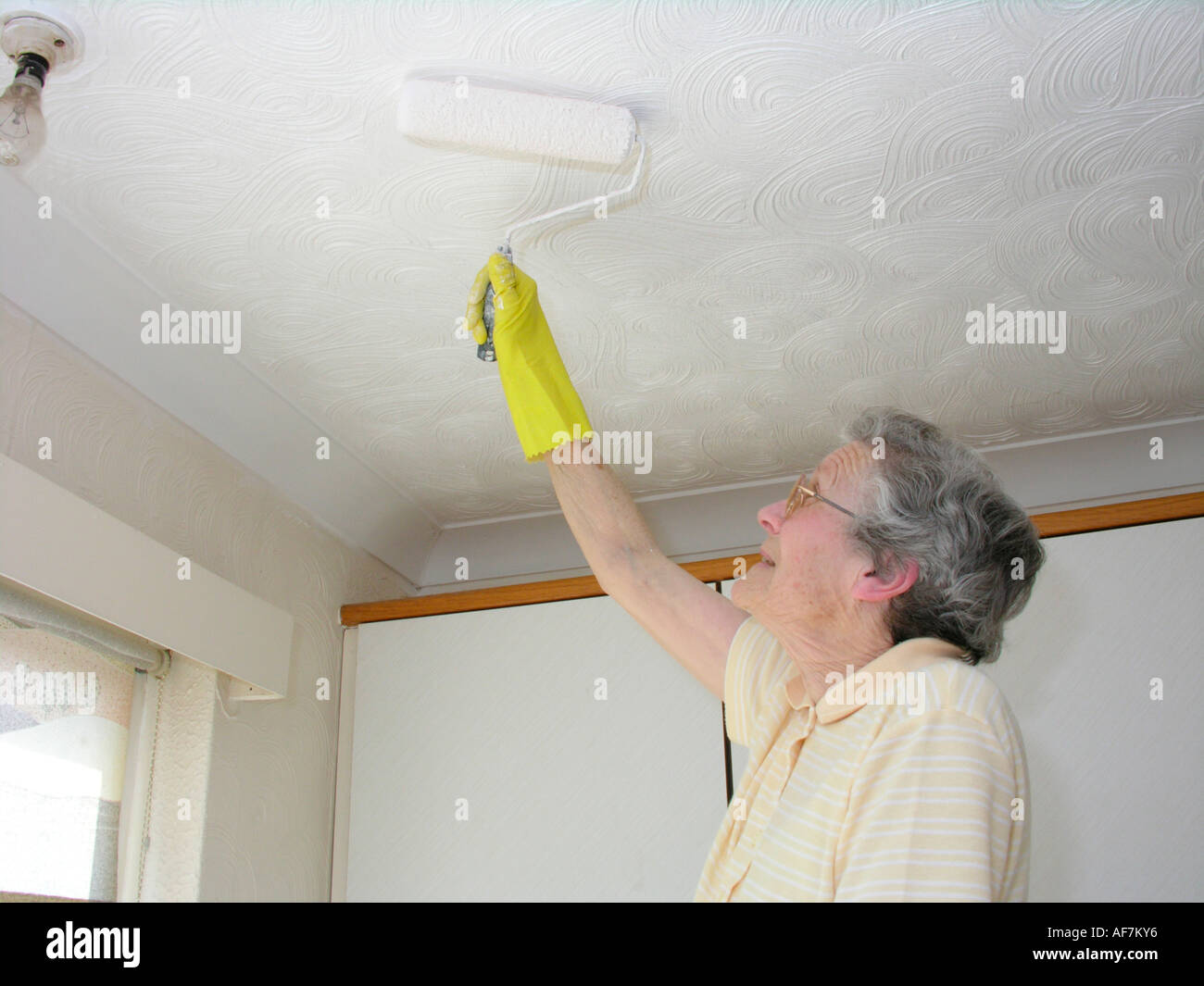 Femme âgée de la décoration et de la peinture du plafond avec un rouleau à peindre et d'avoir à se pencher sur les raccords fixes dans la cuisine Banque D'Images