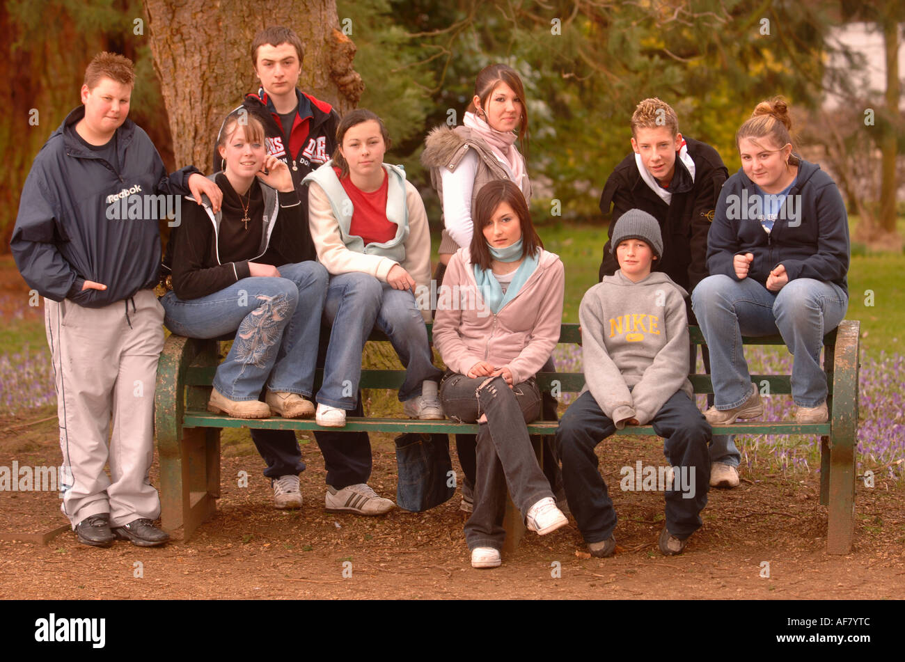 Un GROUPE DE JEUNES GARÇONS ET FILLES ASSIS SUR UN BANC DE PARC UK Banque D'Images