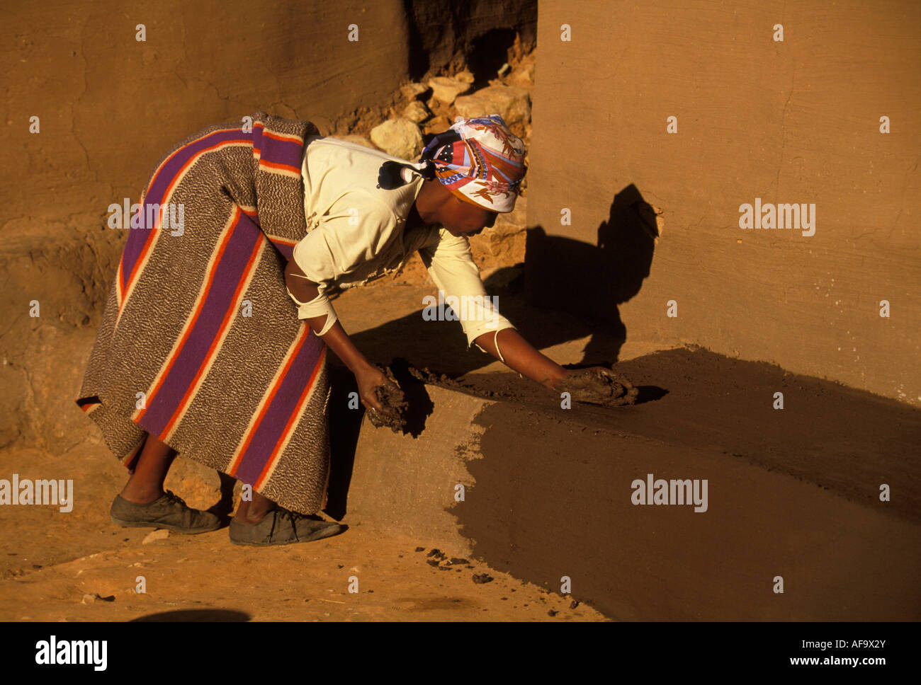 Une femme de réparer ses parois traditionnelles de boue homestead avec boue fraîche. Le Lesotho Banque D'Images