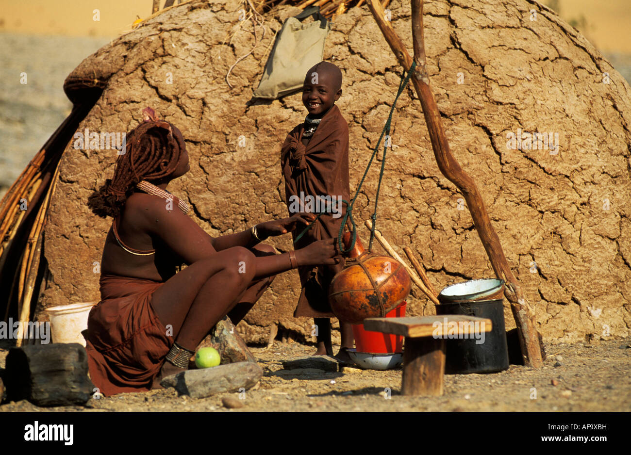 Femme Himba et enfant faisant de crème en calebasse en dehors de leur hutte de terre en forme de dôme, de la rivière Kunene Namibie Kaokoveld ; Banque D'Images