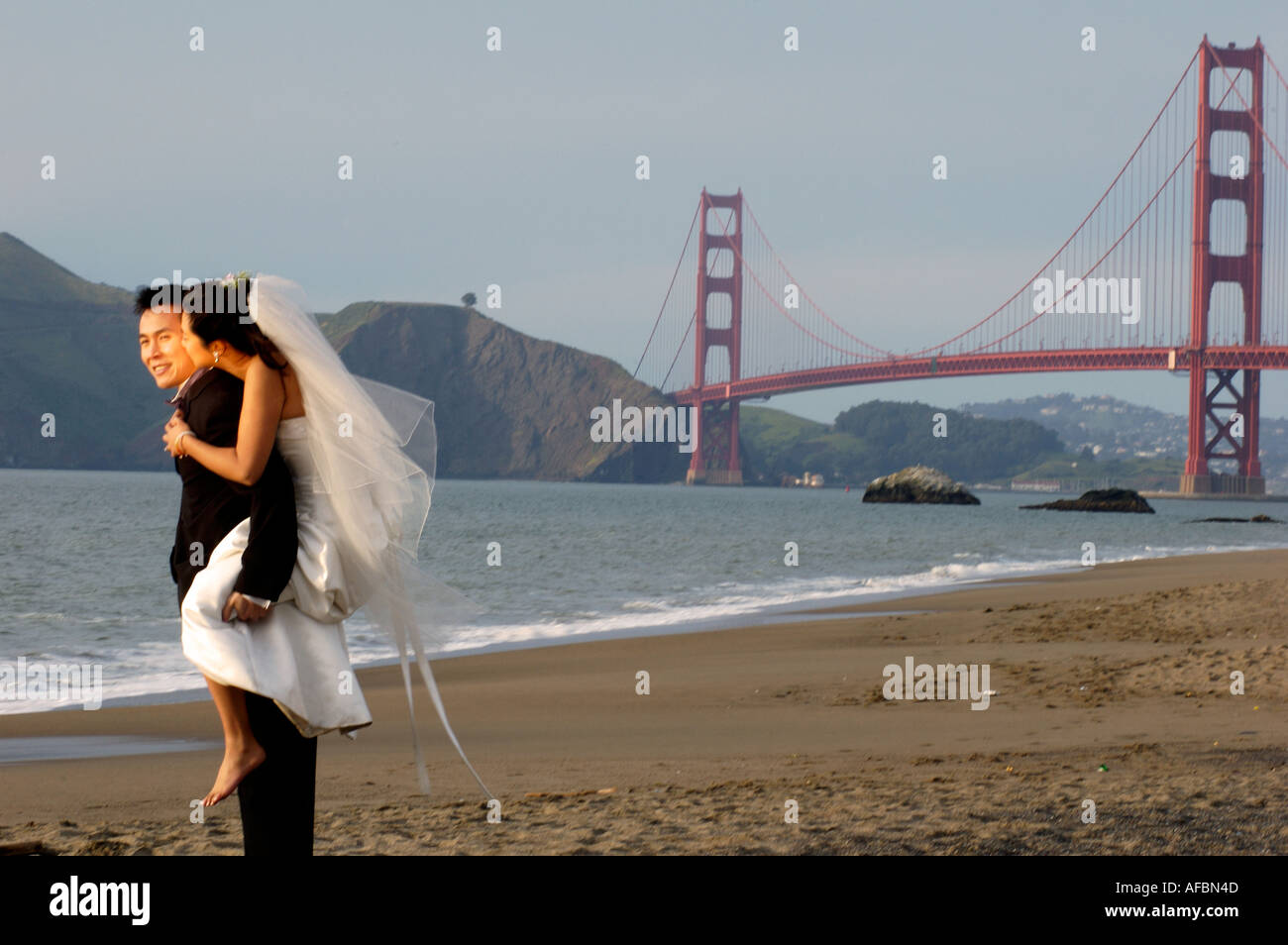 Marié mariée donnant Piggy Back Ride sur Baker Beach à San Francisco Californie le Golden Gate Bridge Banque D'Images