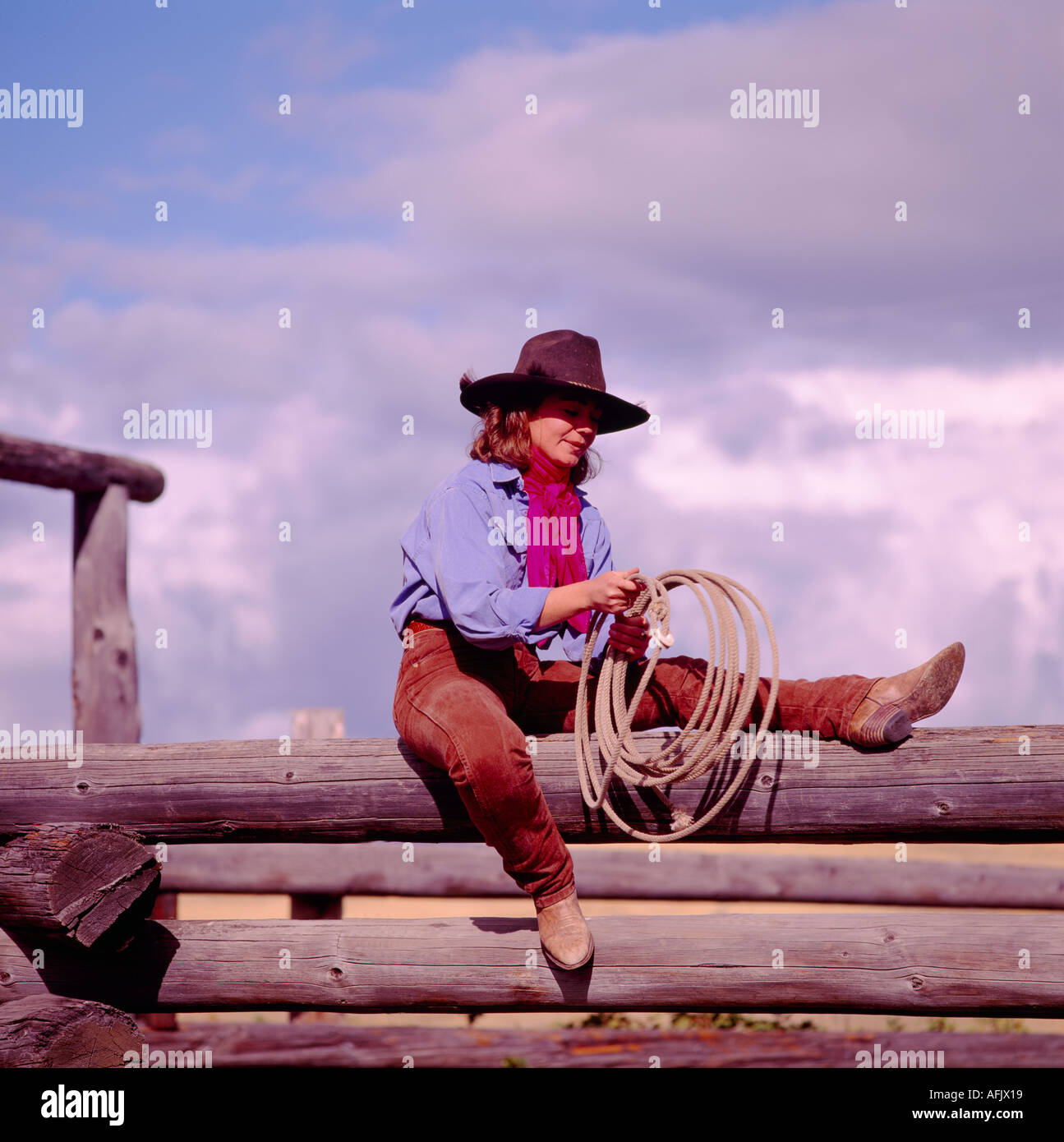 Une Cowgirl sitting on a log Clôture dans la région de Cariboo en Colombie-Britannique, Canada Banque D'Images
