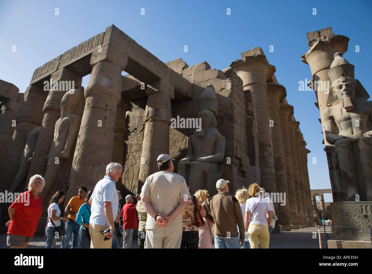 Un groupe touristique est à l'écoute de leur guide sous le regard de Ramsès II à Louxor, Égypte. Banque D'Images