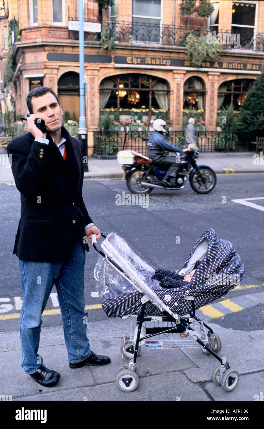 1980s Man UK. Père poussant bébé buggy enfant dans la poussette. Faire un appel téléphonique sur son téléphone portable rétro circa 1985 Mayfair Londres Angleterre HOMER SYKES Banque D'Images