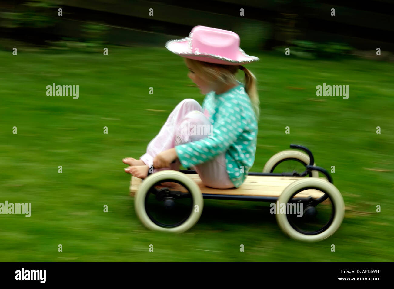 4 ans, Fille en rose cowboy hat équitation un buggy ou kart à la vitesse sur l'herbe Banque D'Images