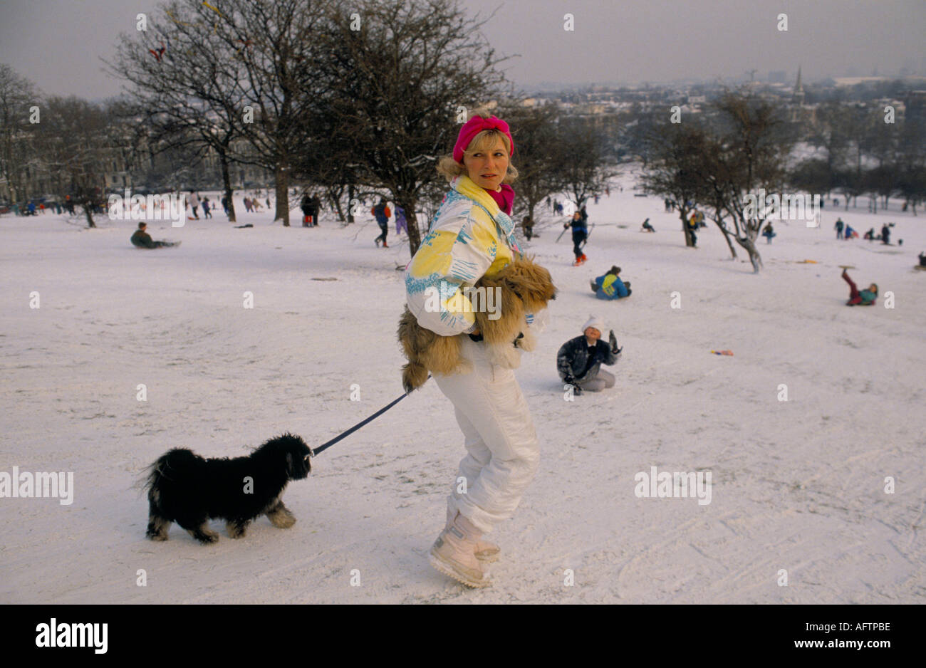 Femme d'âge moyen à la mode promenant un chien portant un autre dans la neige sur Primrose Hil, Londres, Angleterre 1991 1990s UK HOMER SYKES Banque D'Images Femme d'âge moyen à la mode promenant un chien portant un autre dans la neige sur Primrose Hil, Londres, Angleterre 1991 1990s UK HOMER SYKES Banque D'Images