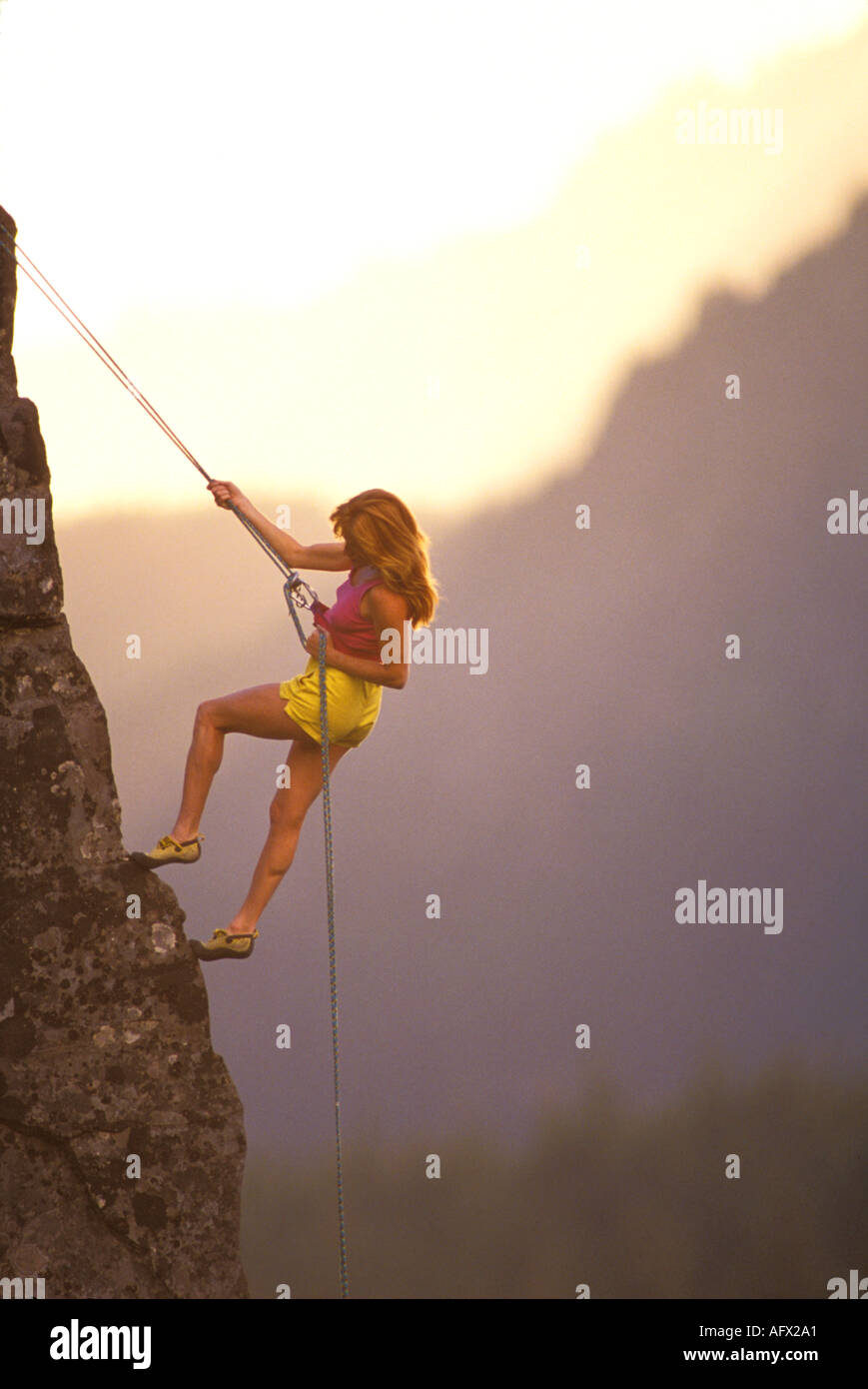 Une femme aux cheveux rouge rock climber rappells en bas d'une paroi rocheuse au coucher du soleil Banque D'Images