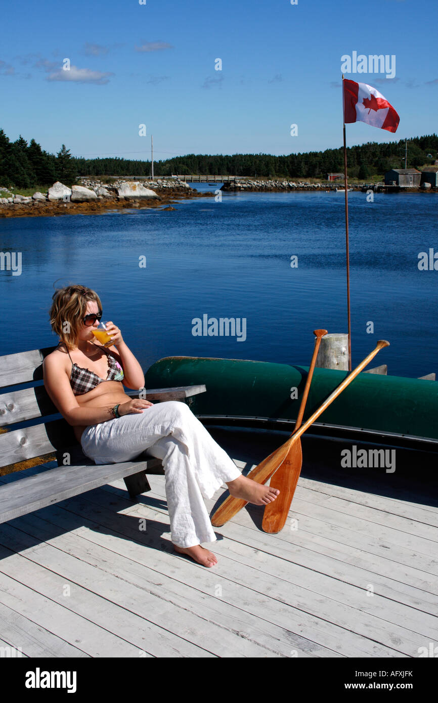 Adolescente avec un verre, prendre un bain de soleil sur un banc sur la jetée de l'Adirondack, Nova Scotia, Canada. Photo par Willy Matheisl Banque D'Images