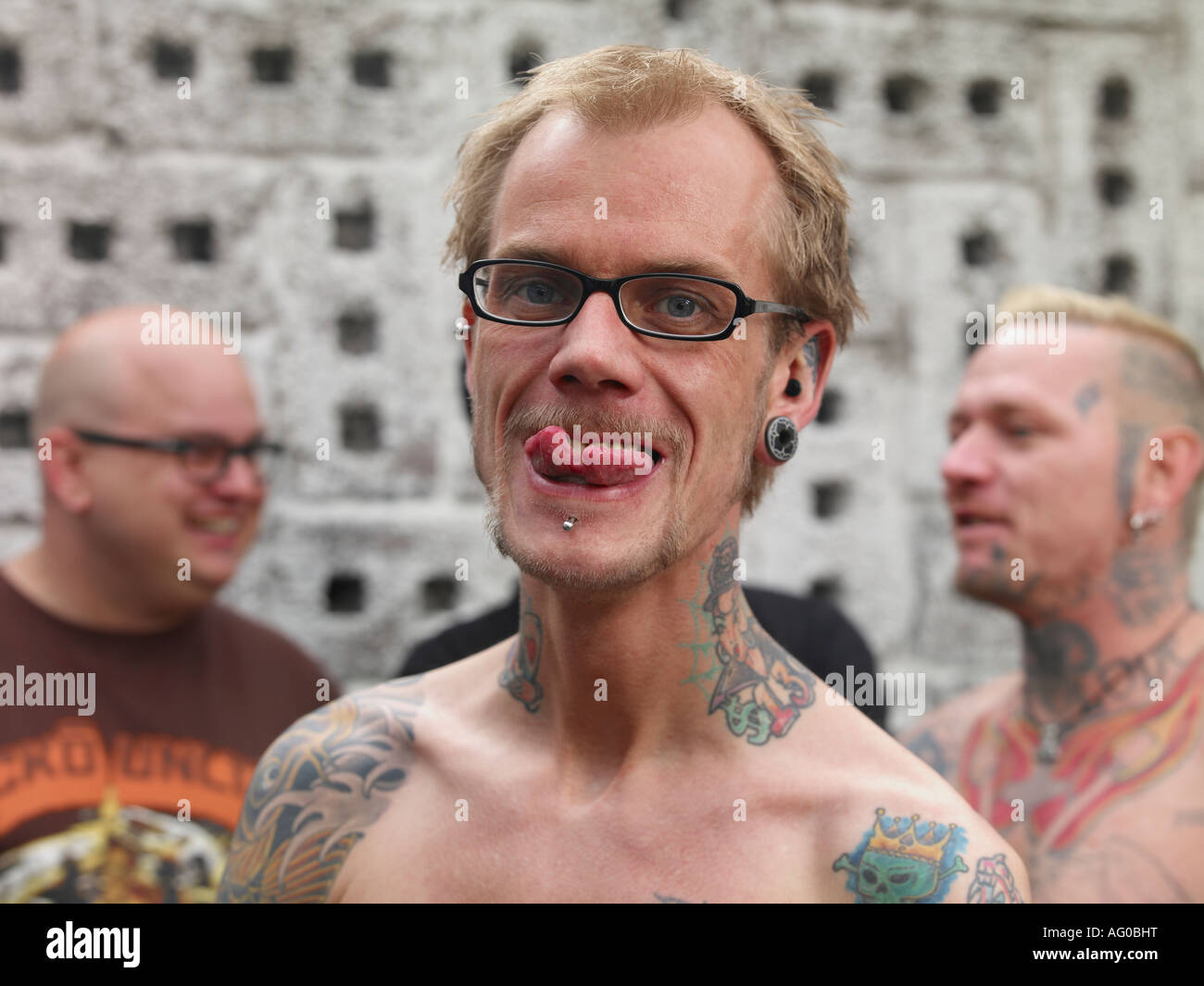 Homme tatoué avec langue piercée et renversé 2 mâles en arrière-plan, Reykjavik Islande Banque D'Images