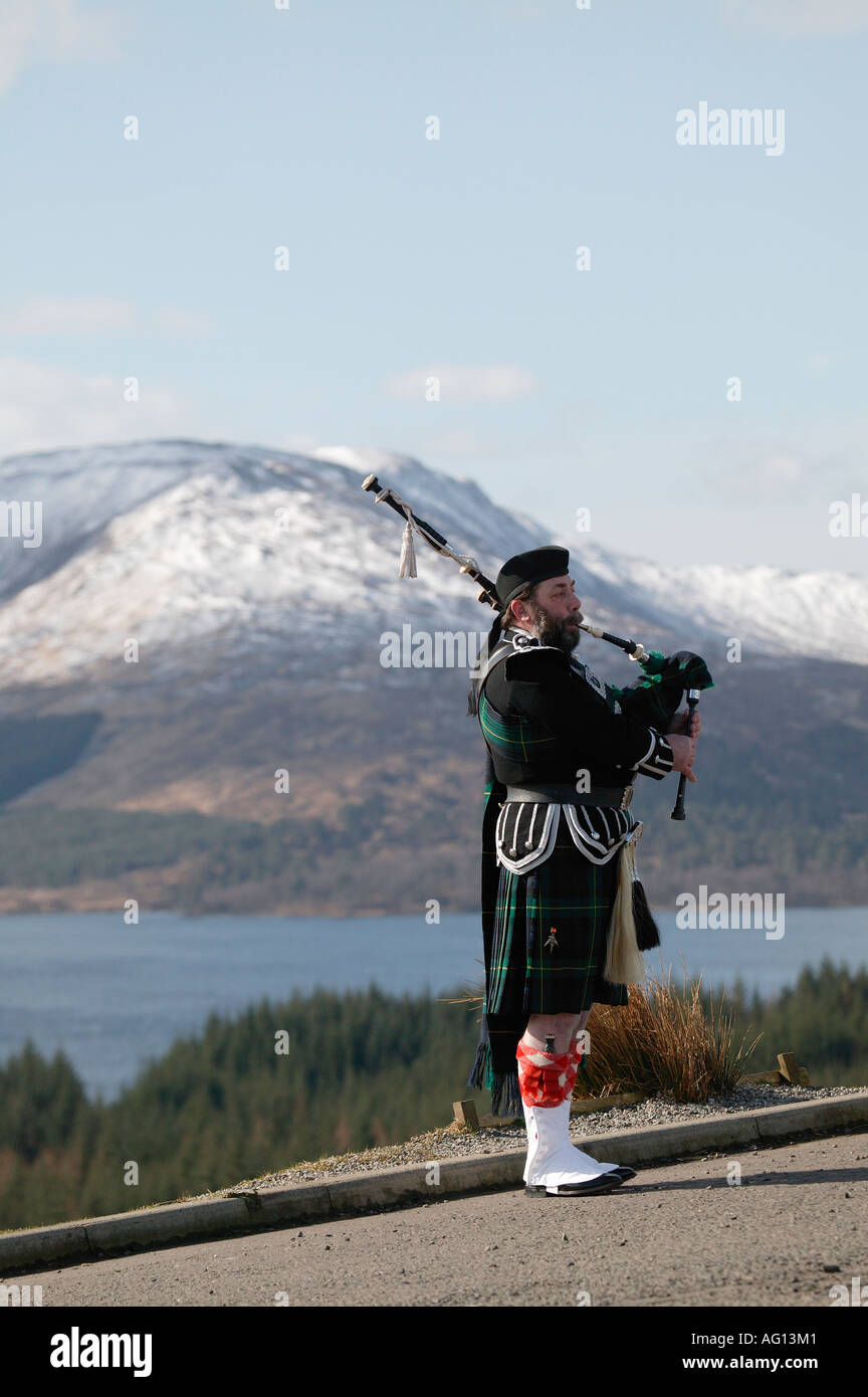 Piper écossais jouer de la cornemuse au-dessus du Loch Tulla, les Highlands écossais, l'Écosse avec une montagne en arrière-plan Banque D'Images