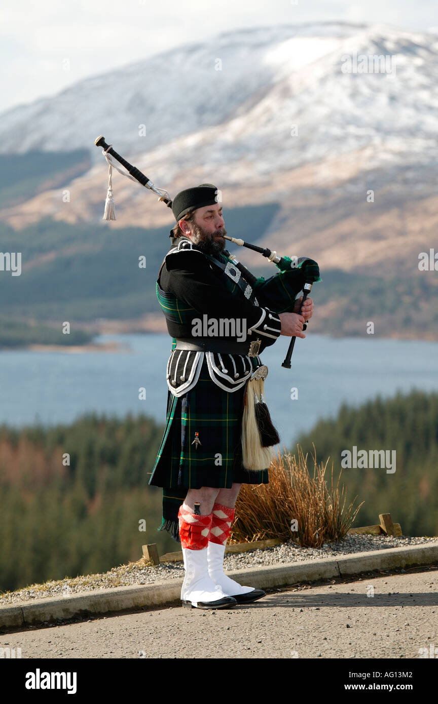 Piper écossais jouer de la cornemuse au-dessus du Loch Tulla, Highlands écossais avec une montagne en arrière-plan Banque D'Images