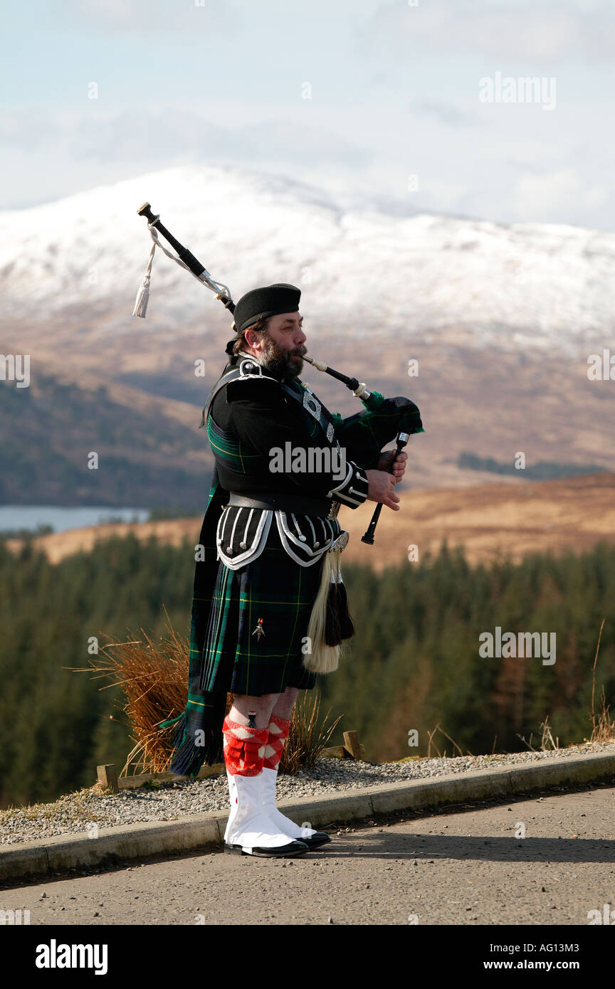 Piper écossais jouer de la cornemuse au-dessus du Loch Tulla, Highlands, Ecosse, avec une montagne en arrière-plan Banque D'Images