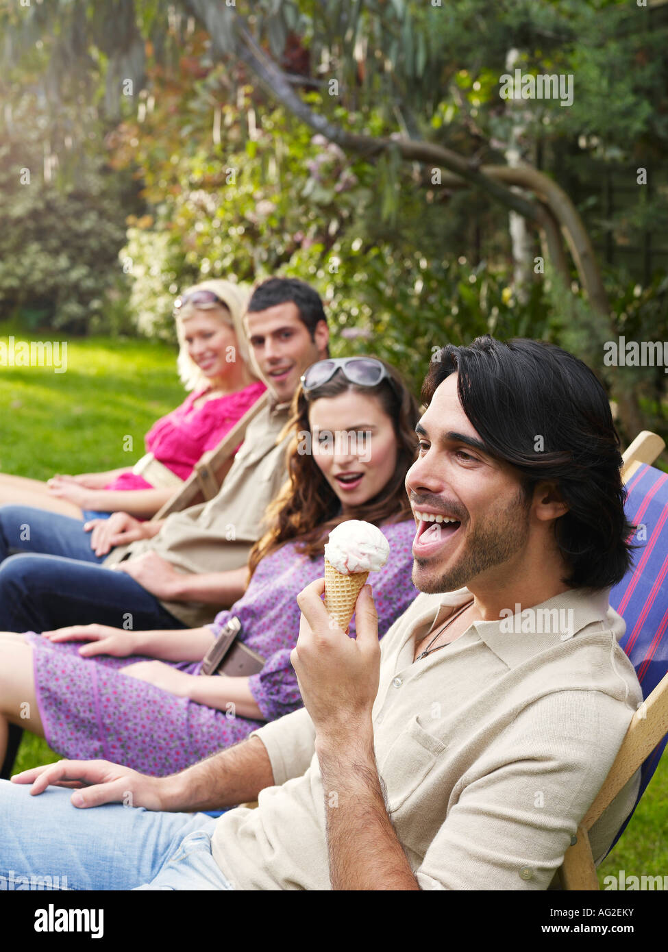 Groupe de jeunes gens assis dans la rangée sur des chaises longues dans le jardin, vue latérale Banque D'Images