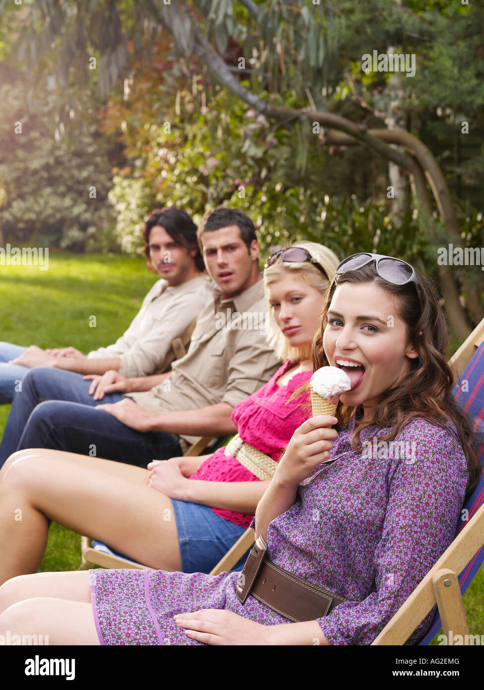 Groupe de jeunes gens assis dans la rangée sur des chaises longues dans le jardin, vue latérale Banque D'Images