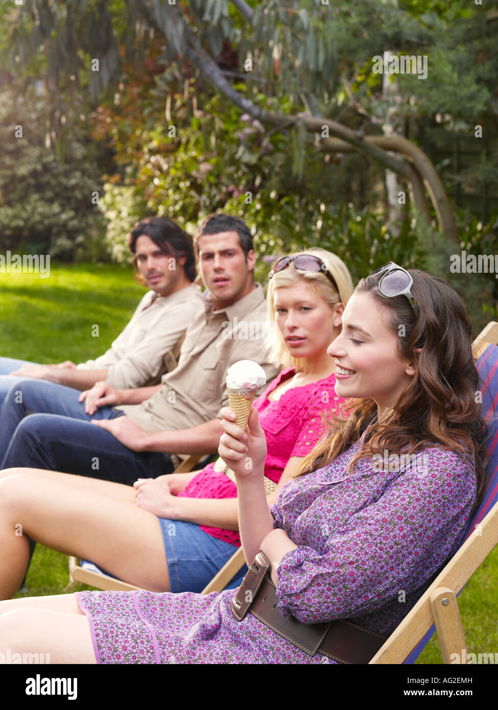 Groupe de jeunes gens assis dans la rangée sur des chaises longues dans le jardin, vue latérale Banque D'Images