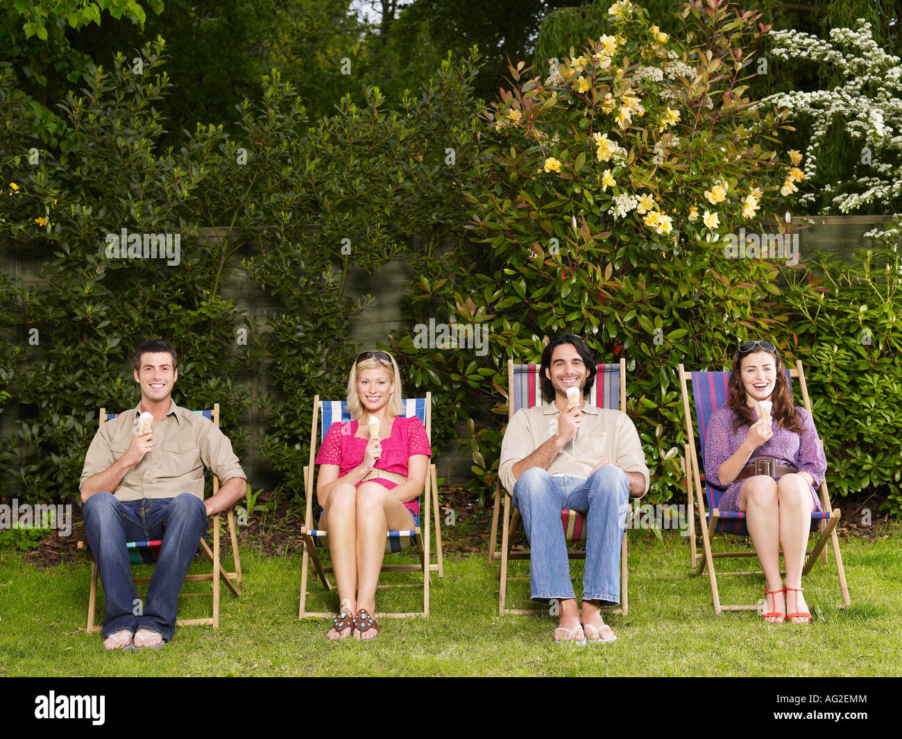Groupe de jeunes gens assis dans la rangée sur des chaises longues dans le jardin, manger des glaces Banque D'Images