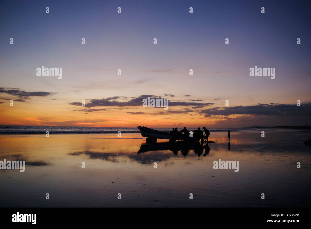 Pousser les pêcheurs à bord de leur bateau en mer au coucher du soleil Banque D'Images