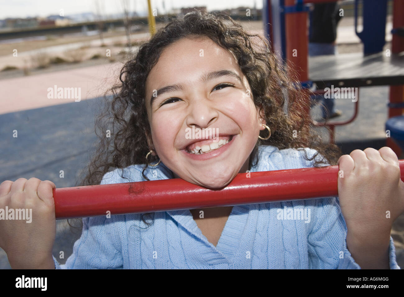 Dix ans, fille accroché à bar sur cour de l'école, grand sourire à pleines dents lumineuses Banque D'Images