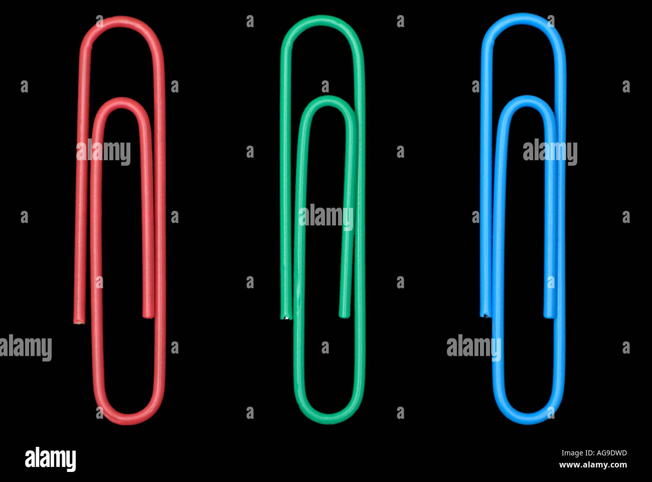 Trombones de bureau contre un fond noir trois objets disposés comme rouge, vert et bleu Banque D'Images