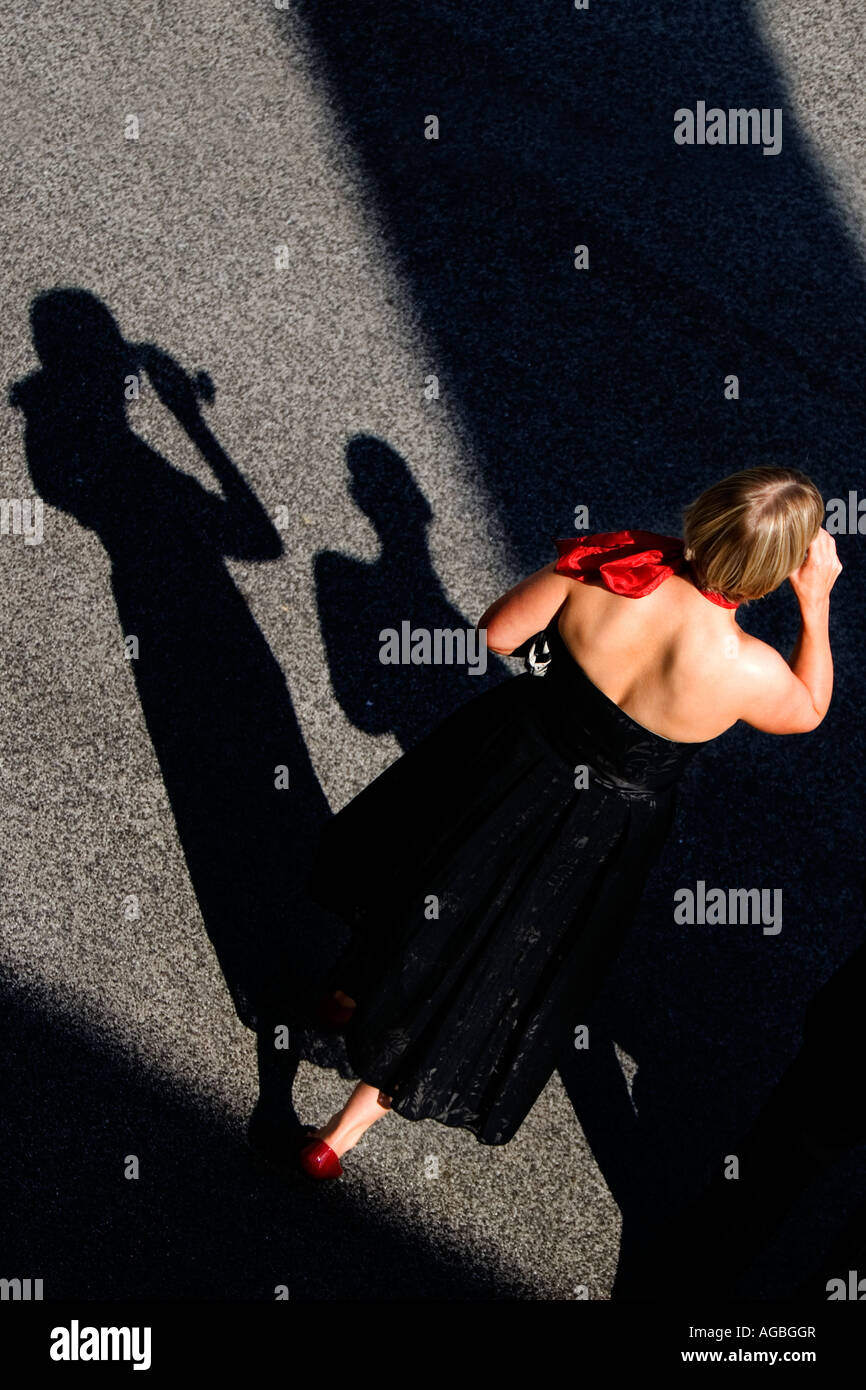 Jeune femme en robe noire et foulard rouge drinking champagne avec une ombre noire et sillouette Banque D'Images